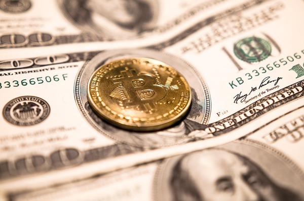 Bitcoin coin resting on US dollar banknotes