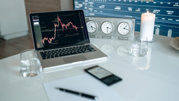 Laptop displaying a candlestick trading chart on a desk with clocks