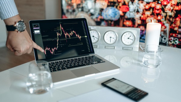 Laptop showing a trading chart next to desk clocks and a candle