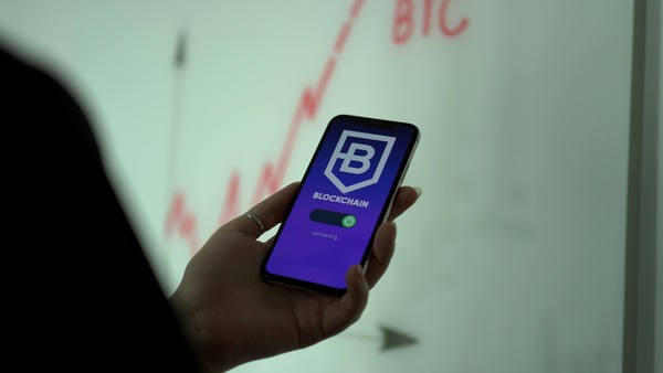 Hand holding a phone displaying a Blockchain app icon with a rising price chart