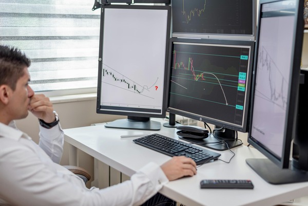Trader analyzing multiple stock chart monitors at a desk